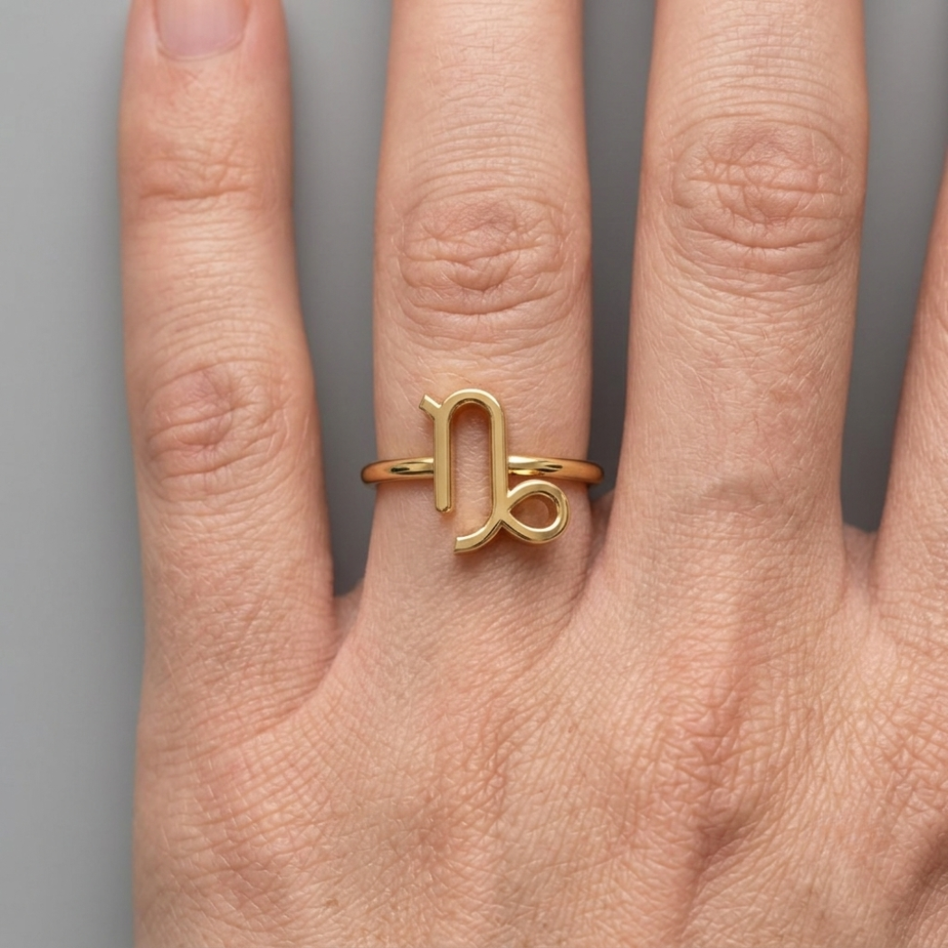 Model's hand resting on fabric wearing Capricorn zodiac ring, soft daylight