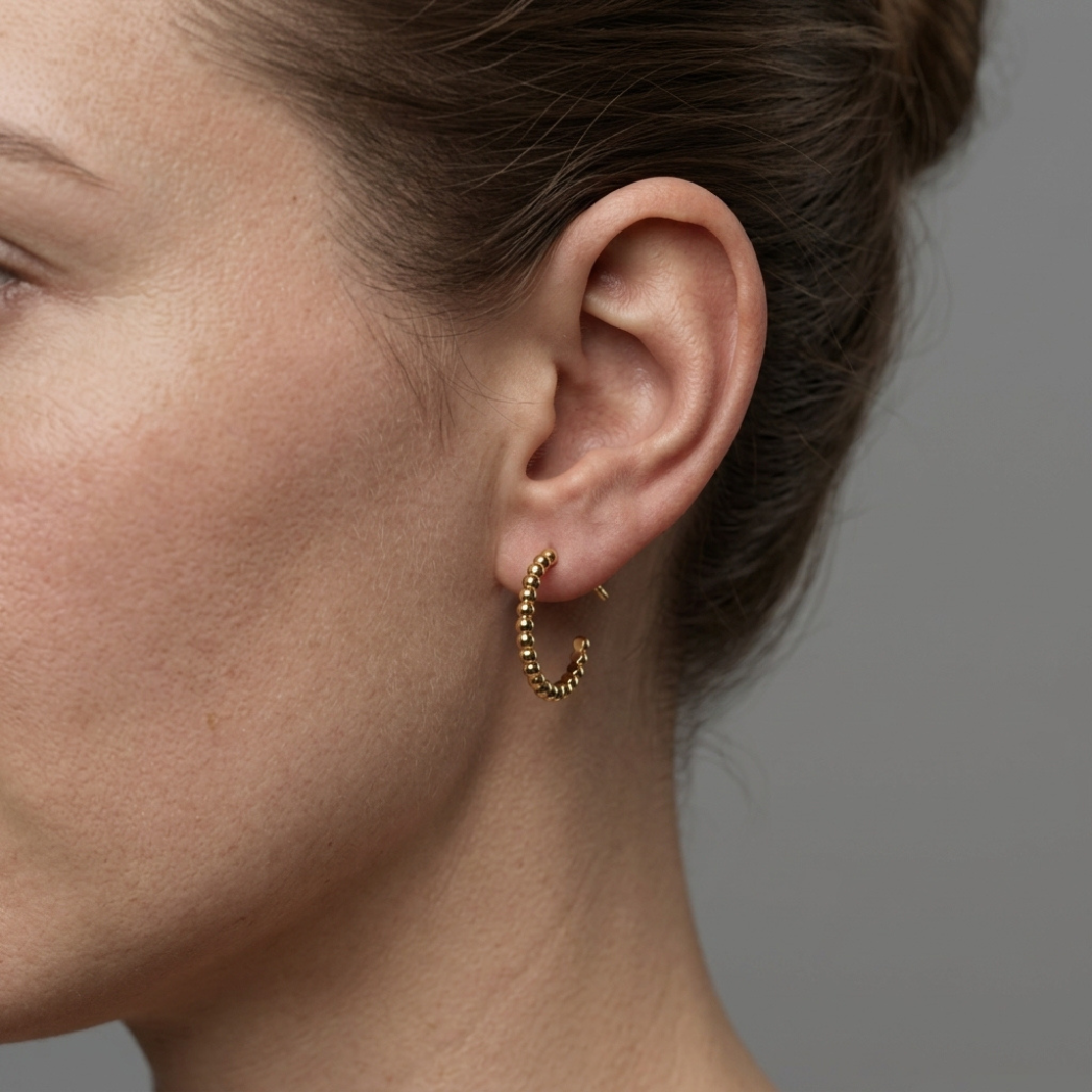 The Aura Pearl Hoops in 14k gold resting on a soft, natural texture, showing the refined luster of the pearls.
