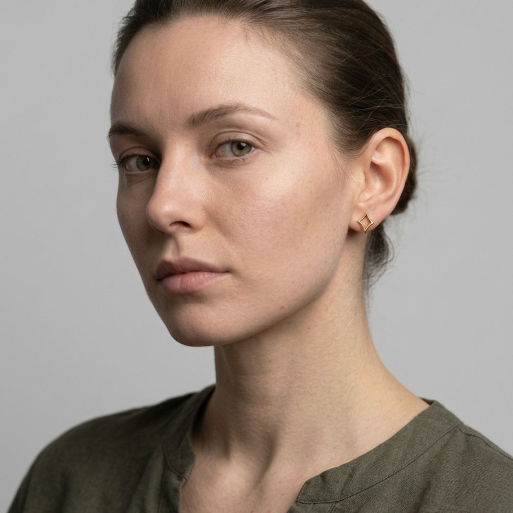 Gold diamond-shape earrings worn on ear, natural light